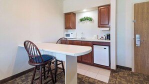 Una cocina compacta con encimera blanca, armarios de madera, microondas, fregadero y un refrigerador pequeño.