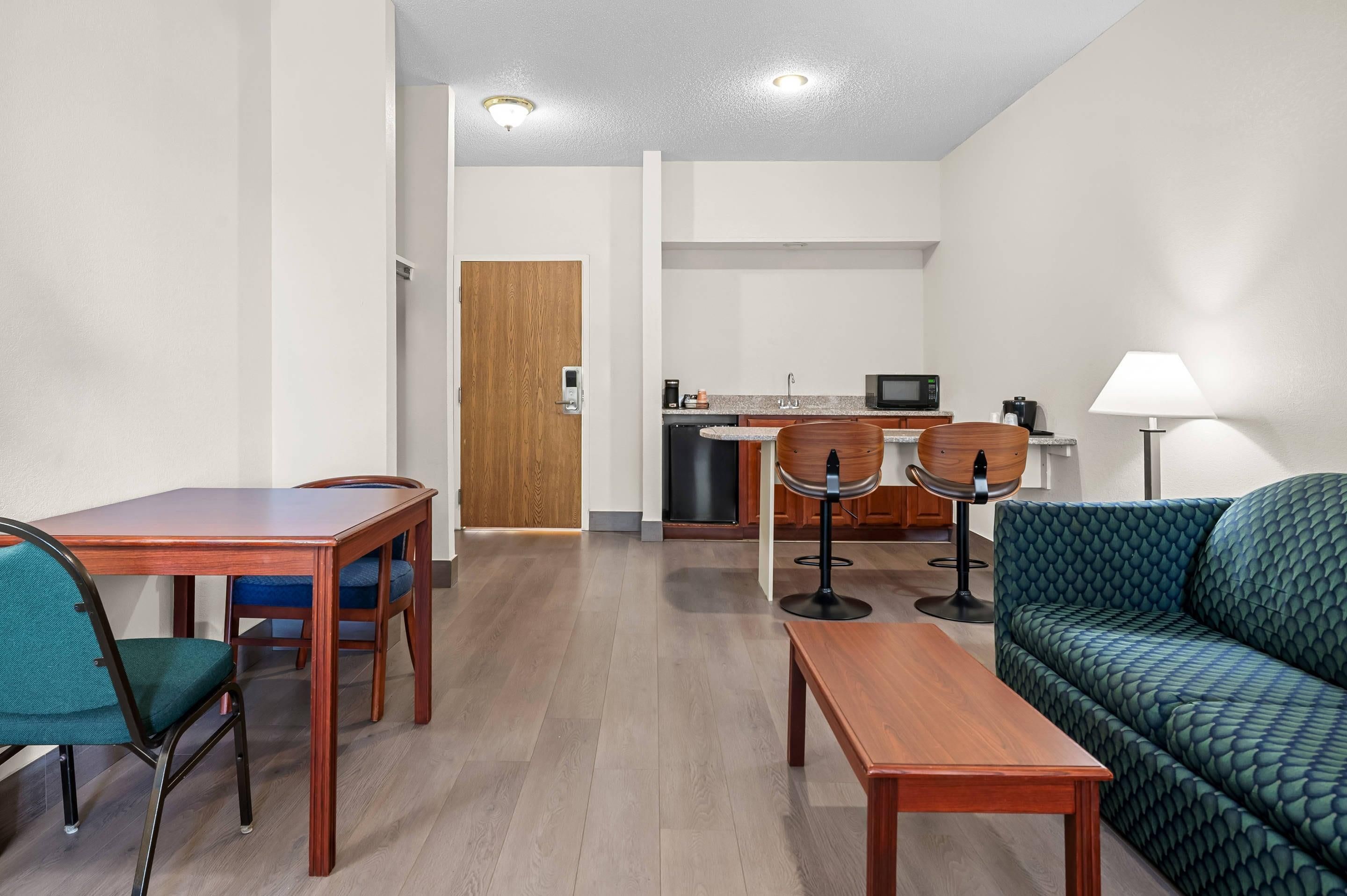 A modern living room with a wooden dining table, a sofa, and a kitchen area with a microwave and sink.