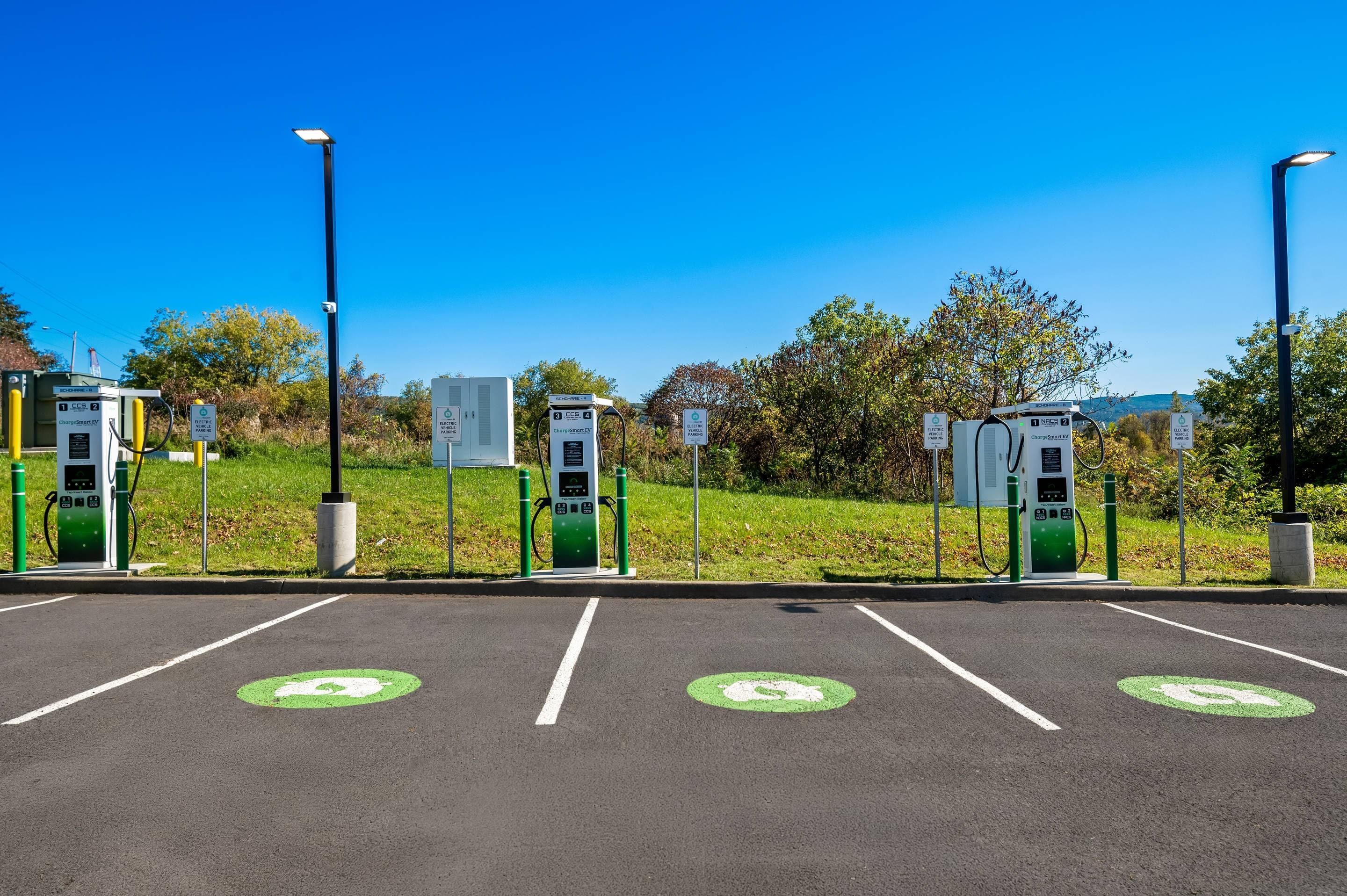A parking area with electric vehicle charging stations, marked parking spaces, and a clear sky.