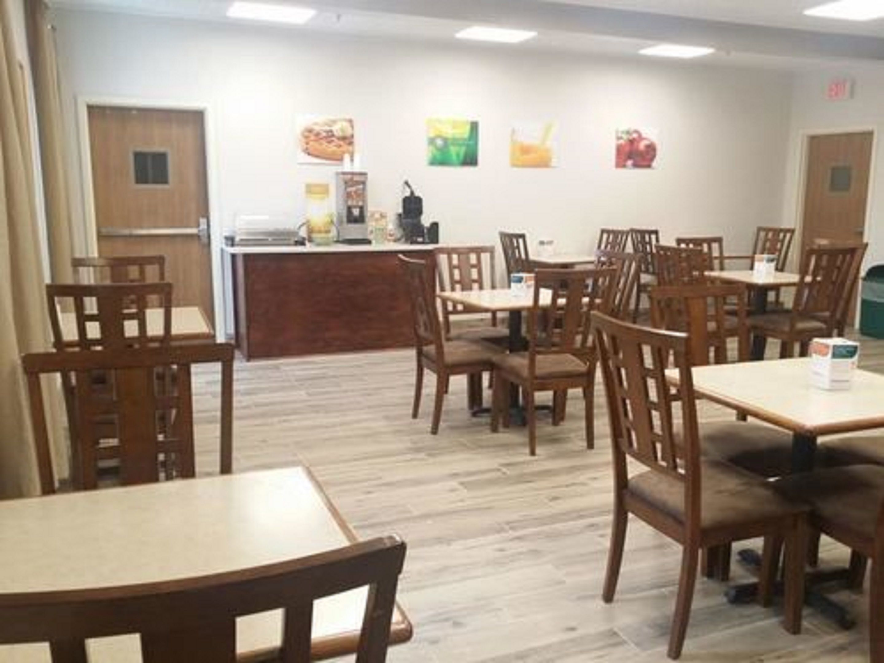 A dining area with wooden tables and chairs, a counter with a coffee machine, and wall art depicting food items.