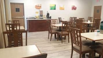 A dining area with wooden tables and chairs, a counter with a coffee machine, and wall art depicting food items.