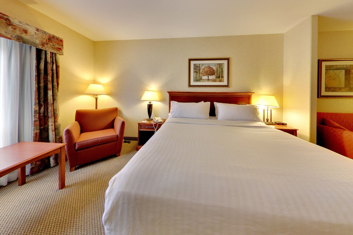 A hotel room with a large bed, two bedside tables with lamps, a chair, and a desk.