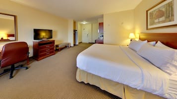 A hotel room with a large bed, a desk with a chair, a television, and a bench.
