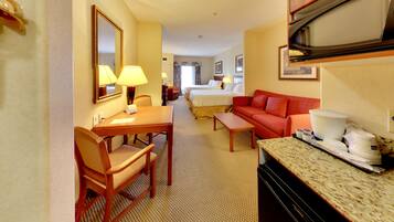 Habitación de hotel con zona de comedor, cama, sofá rojo, espacio de cocina y baño.