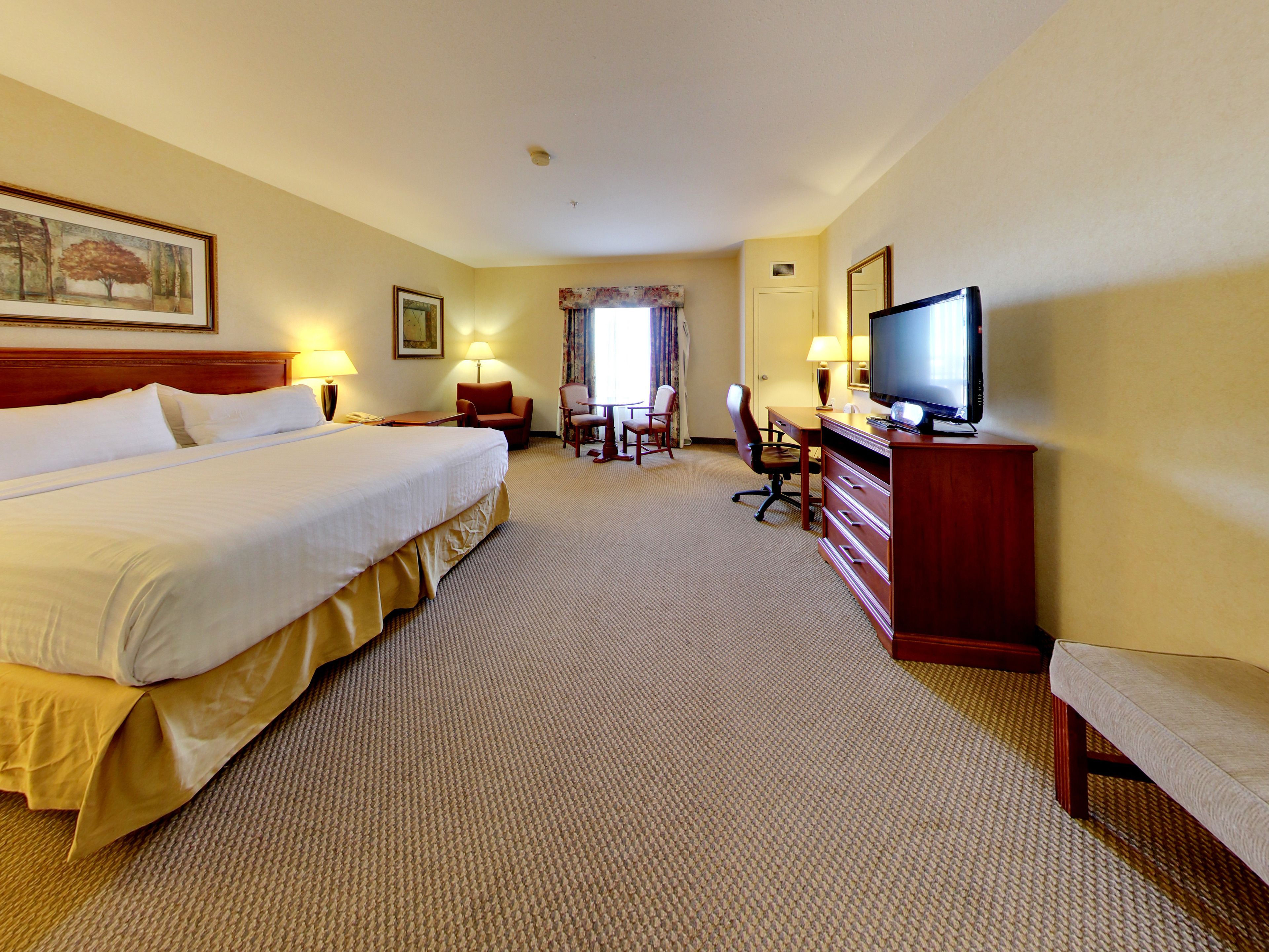 A hotel room with a large bed, a desk with a chair, a television, and a window with curtains.