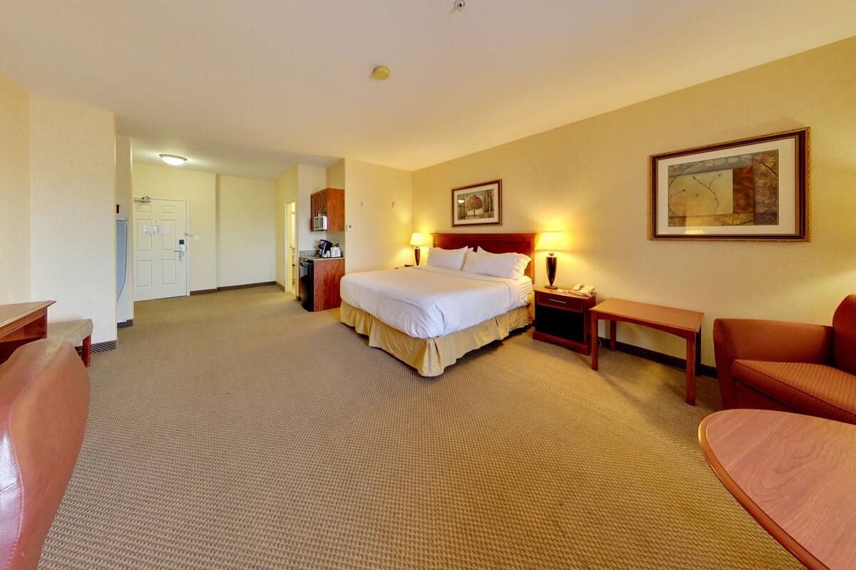 A hotel room with a bed, bedside table, lamp, and a desk with a chair.