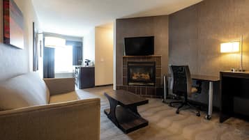 A modern living room with a sofa, a coffee table, a fireplace, a TV mounted above it, and a desk with a lamp.
