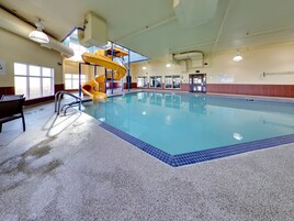Una piscina interior con un tobogán espiral amarillo, agua azul cristalina y un banco junto a la piscina.
