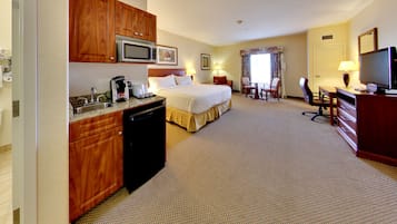 Habitación de hotel con cama, escritorio, televisión, microondas y una pequeña cocina.
