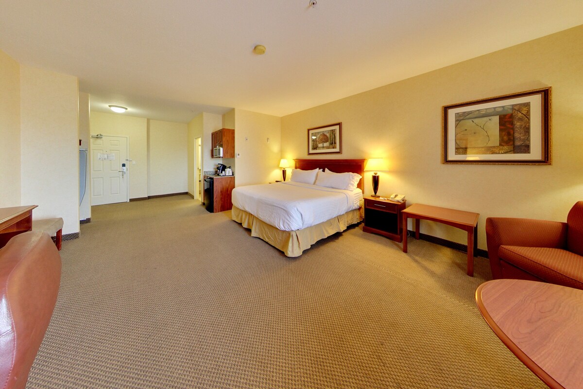 A hotel room with a bed, bedside table, lamp, and a desk with a chair.