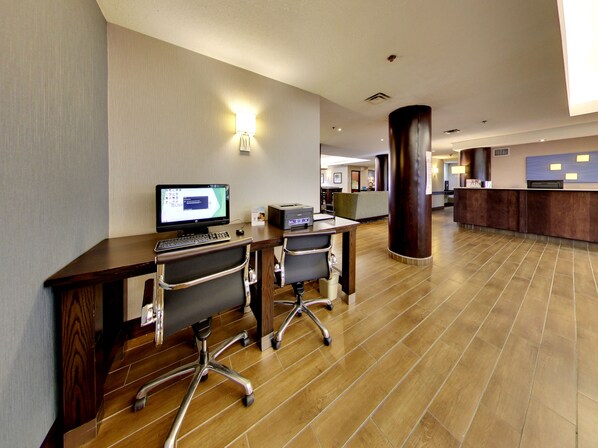 A hotel reception area with a computer desk, two office chairs, a reception desk, and a tiled floor. - Holiday Inn Express & Suites Edmonton International Airport by IHG (Nisku)