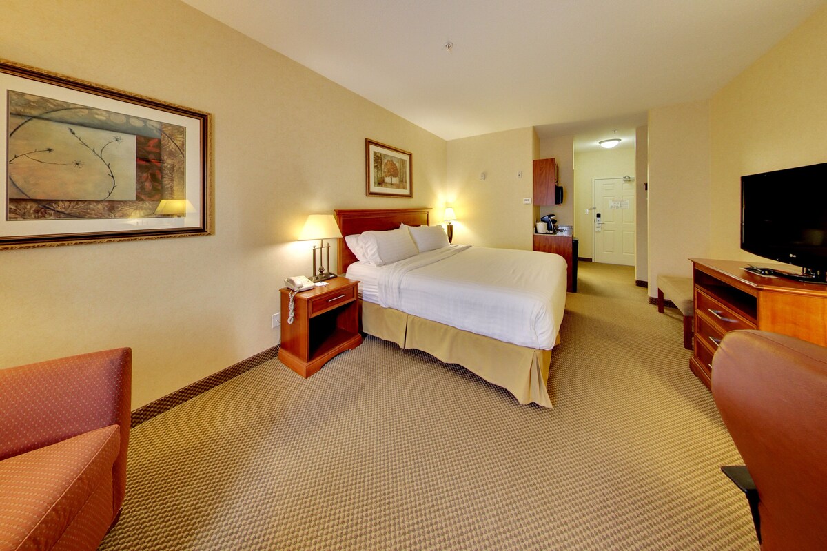 A hotel room with a bed, bedside table, lamp, television, and artwork on the wall.