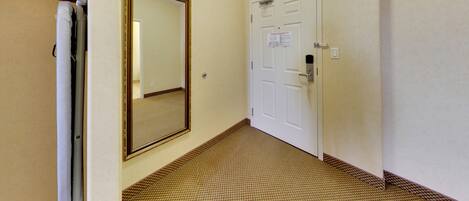 A hallway with a carpeted floor, a white door with a lock, and a large mirror on the wall.