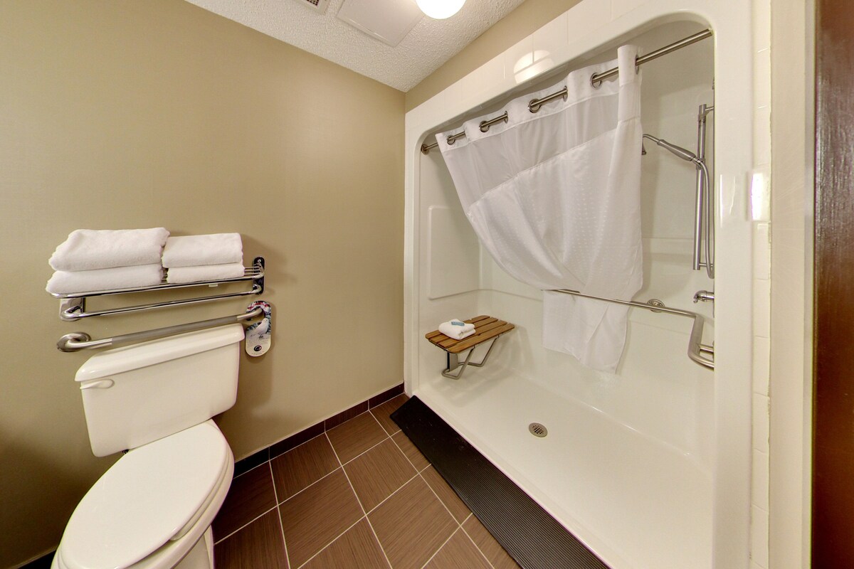 A bathroom with a toilet, a shower with a glass door, and a towel rack with folded towels.