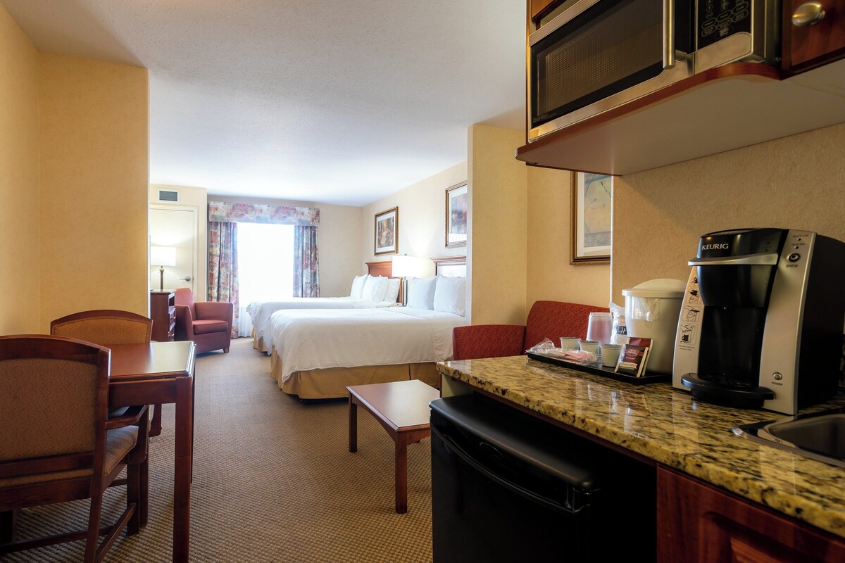 A hotel room with a kitchenette, a bed, a desk, and a chair.