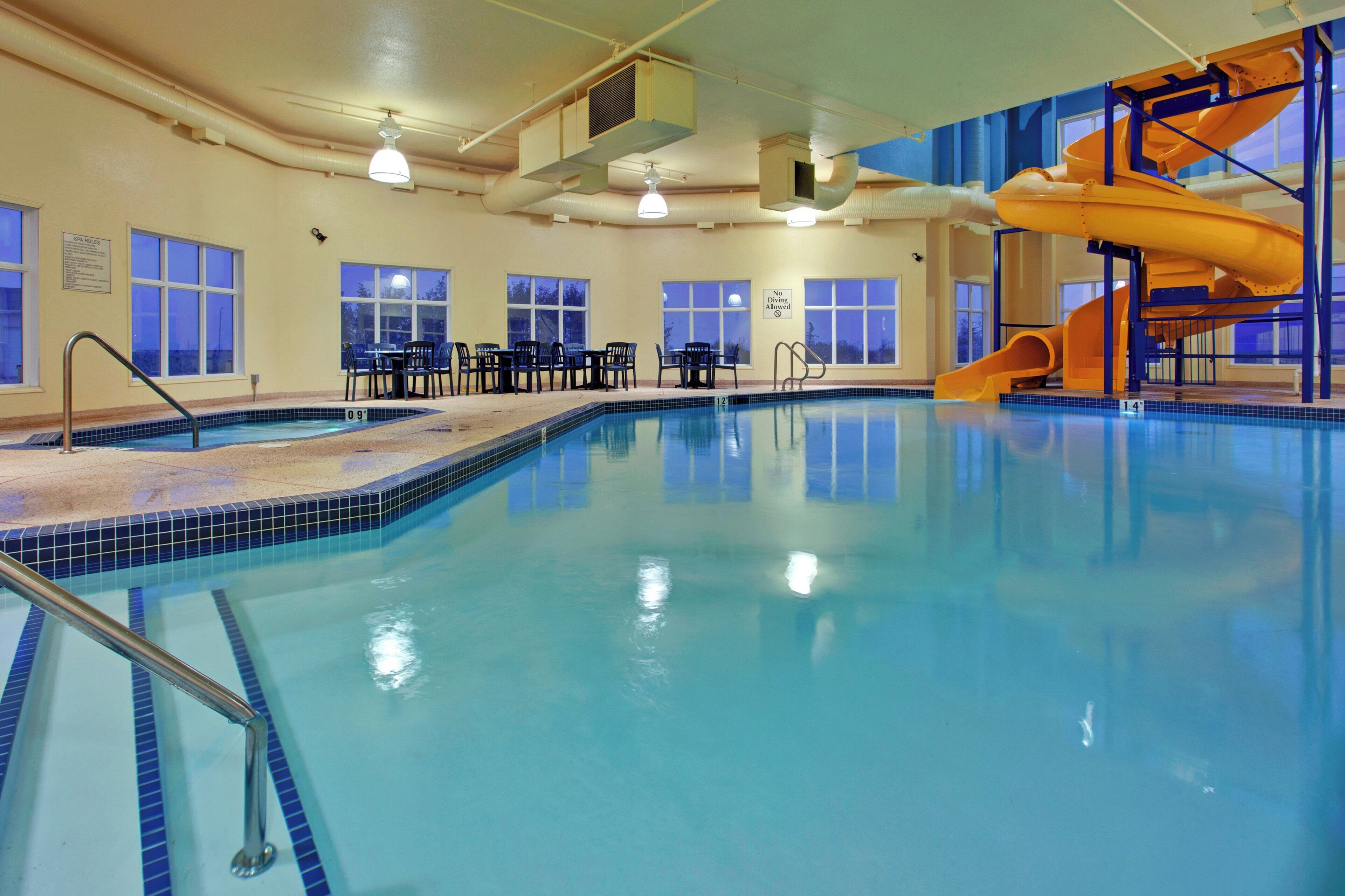Une piscine intérieure avec un toboggan, des chaises et des tables.