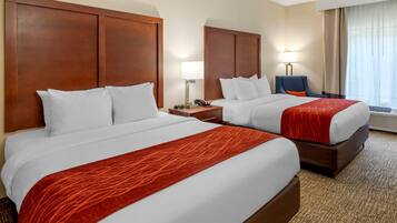 Et hotelværelse med to senge, et skrivebord, en stol og et vindue med gardiner.