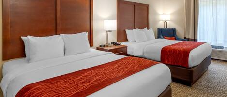 Una habitación de hotel con dos camas, un escritorio, una silla y un ventanal con cortinas.