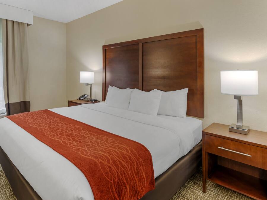 Una habitación de hotel con una cama grande, dos mesitas de noche, una lámpara y una ventana con cortinas.