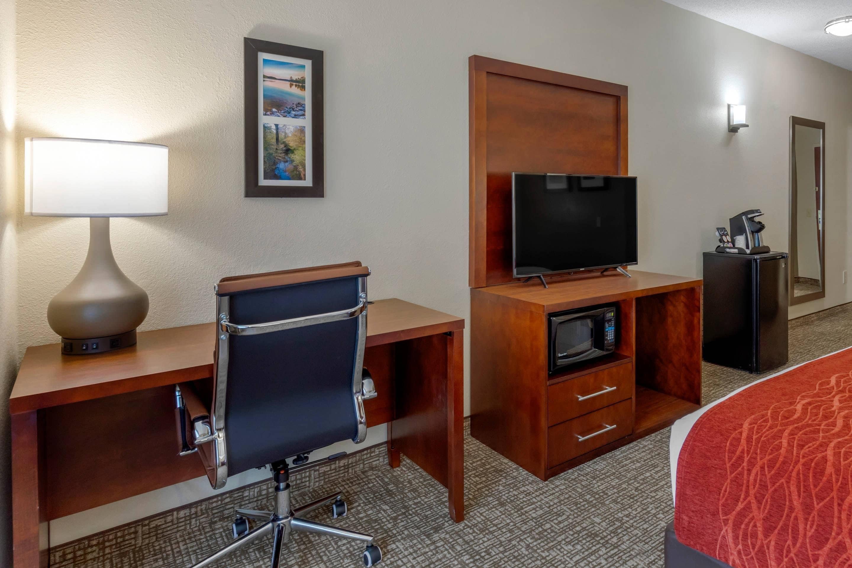 A hotel room with a desk, chair, television, microwave, and a bed with a red blanket.