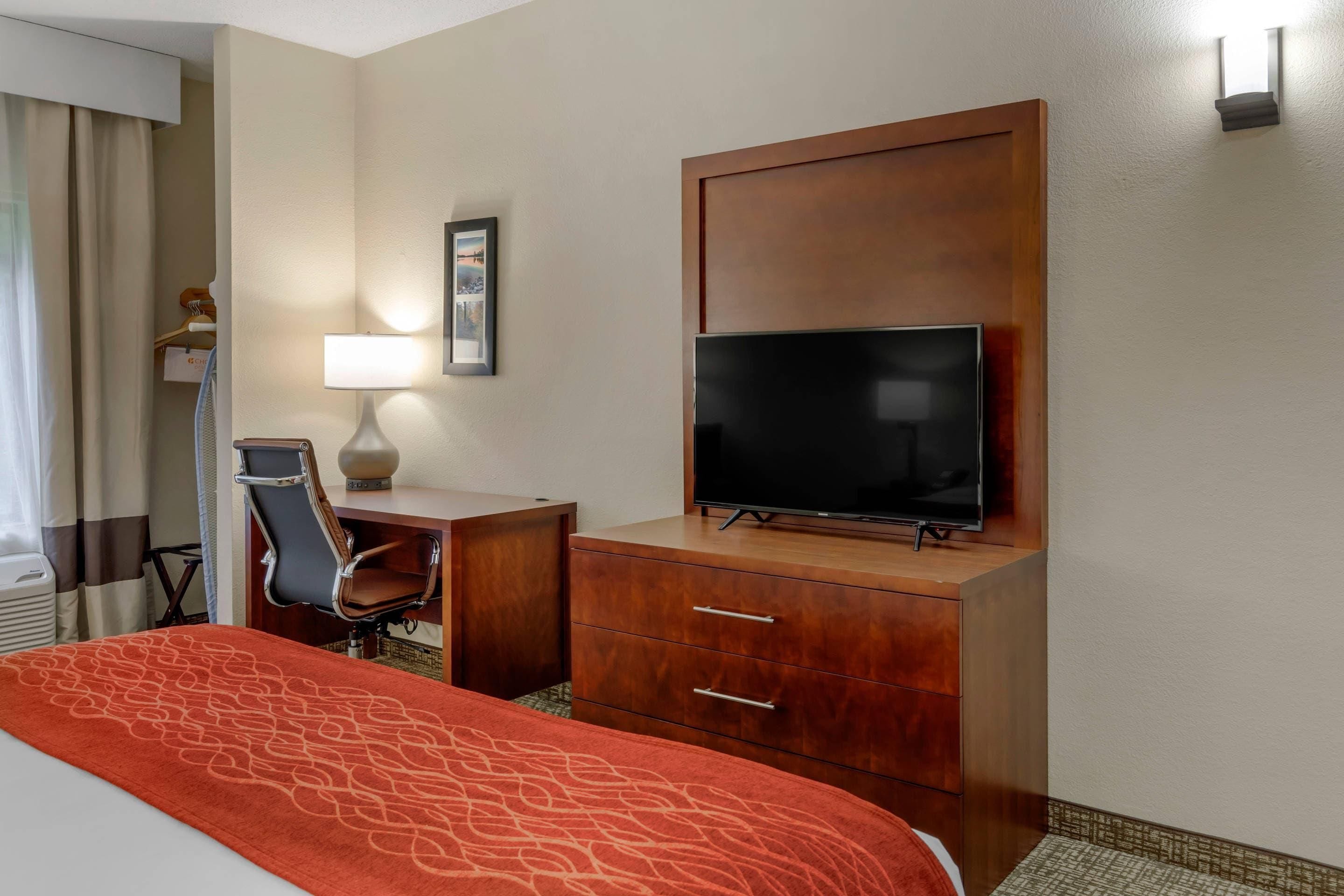 Una habitación de hotel con una cama, un escritorio con una silla, un televisor y un estante en la pared.