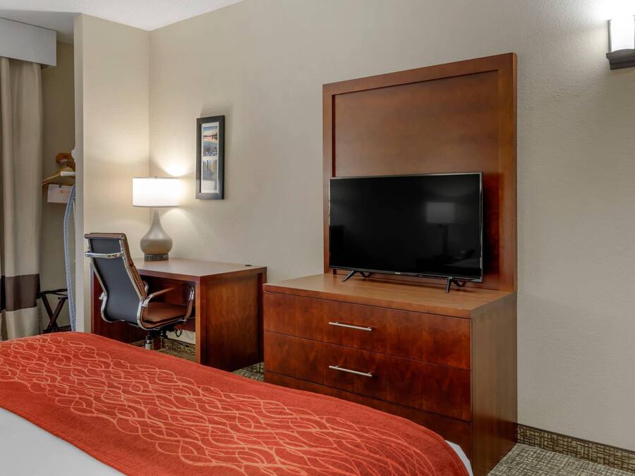Una habitación de hotel con una cama, un escritorio con una silla, un televisor y un estante en la pared.