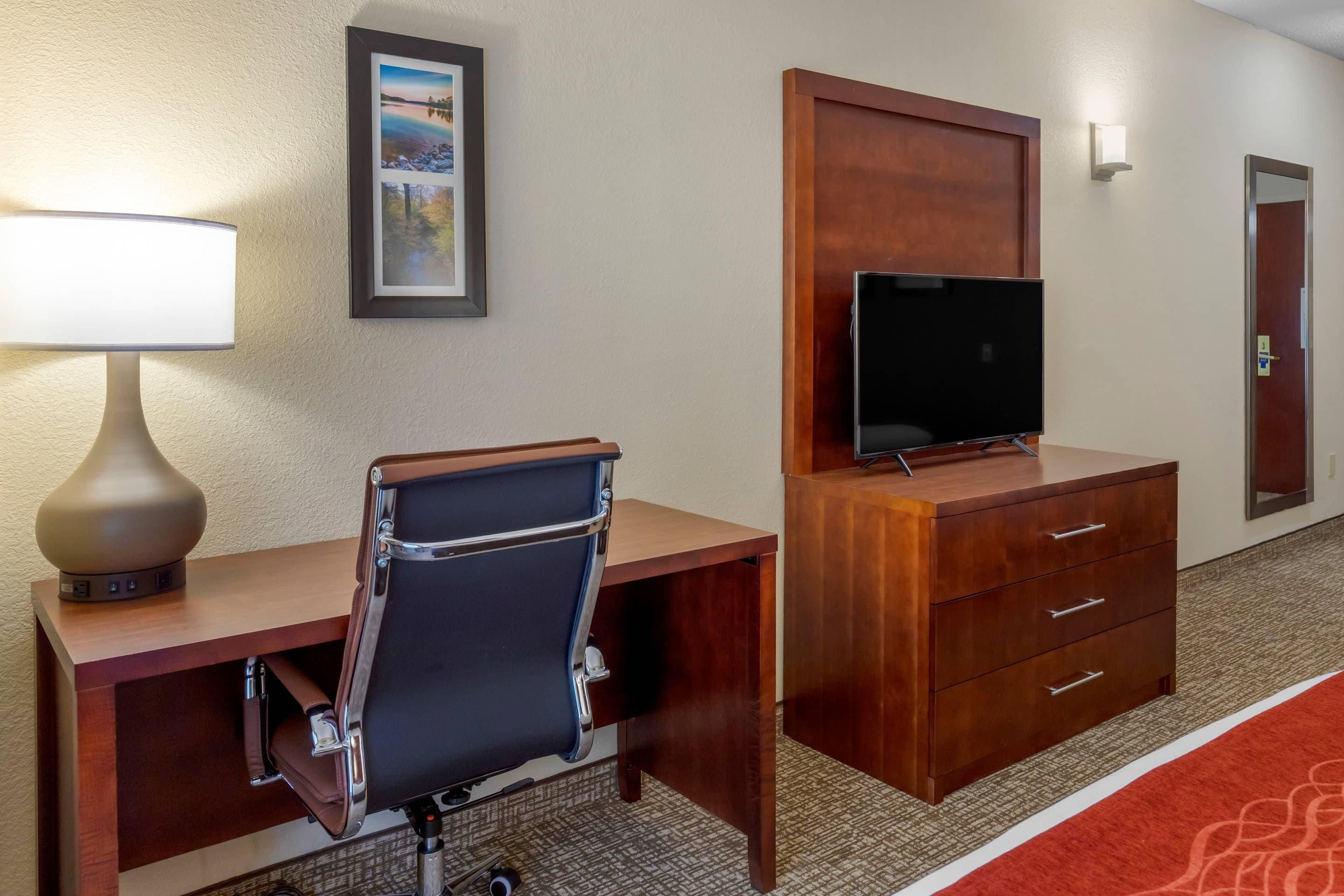 A hotel room with a desk, chair, television, and a mirror.