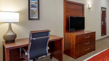 A hotel room with a desk, chair, television, and a mirror.