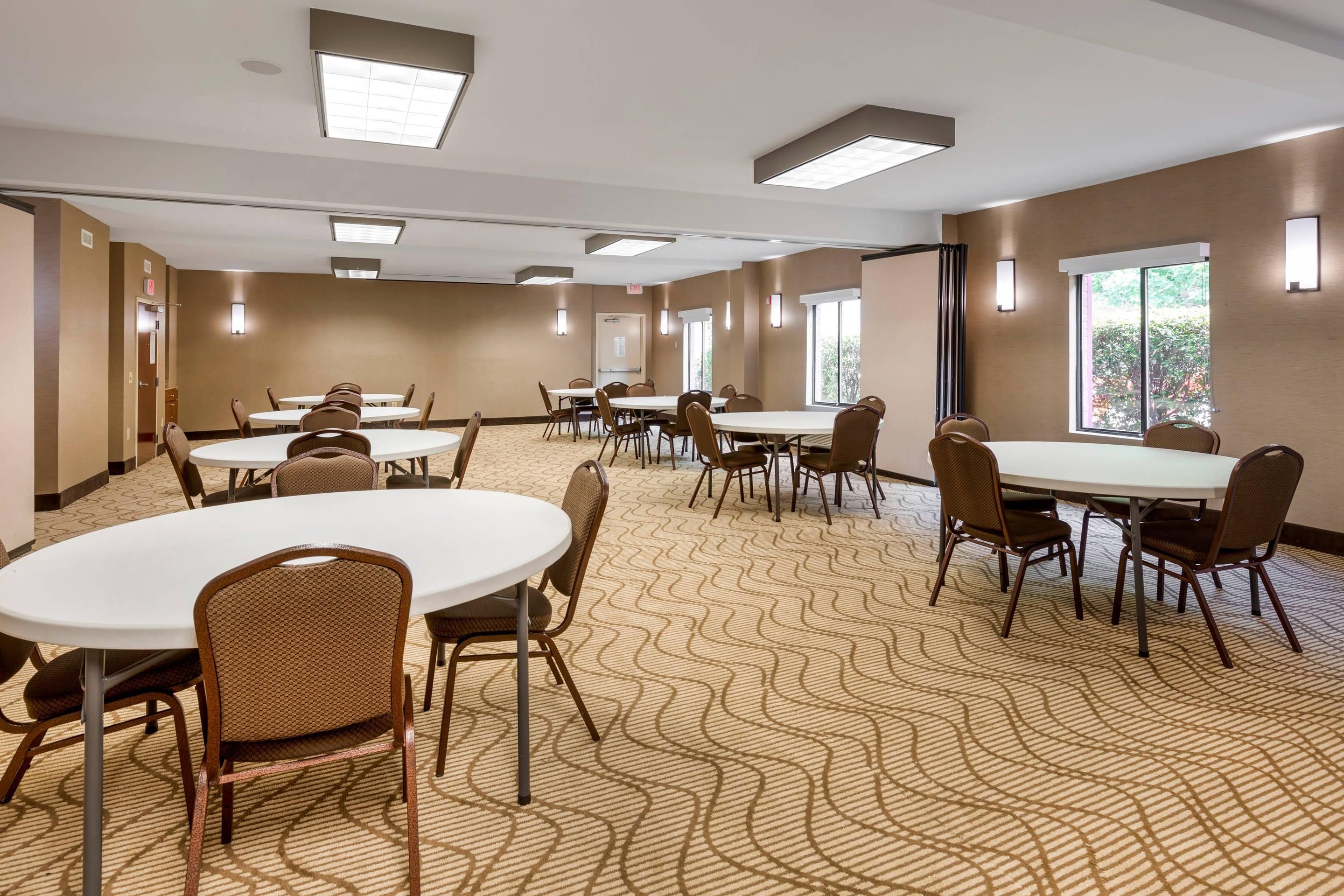 Une salle de conférence dotée de plusieurs tables et chaises, de grandes fenêtres et d’un tapis à motifs.