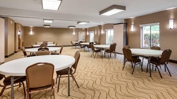 Une salle de conférence dotée de plusieurs tables et chaises, de grandes fenêtres et d’un tapis à motifs.