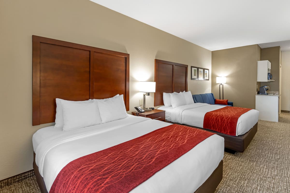 A hotel room with two beds, a desk, a lamp, and a minibar.