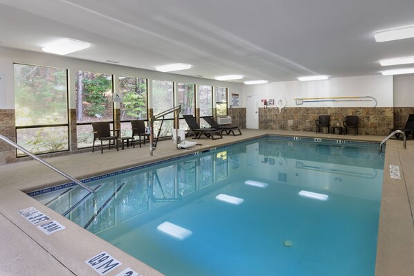 Una piscina con sillas de descanso, un vestuario y grandes ventanales con vistas al bosque.