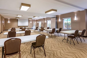 Un salón de conferencias con varias mesas y sillas, una pantalla de proyector y ventanas grandes.