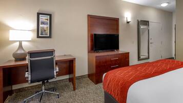 A hotel room with a desk, chair, television, wardrobe, and a bed with a red blanket.