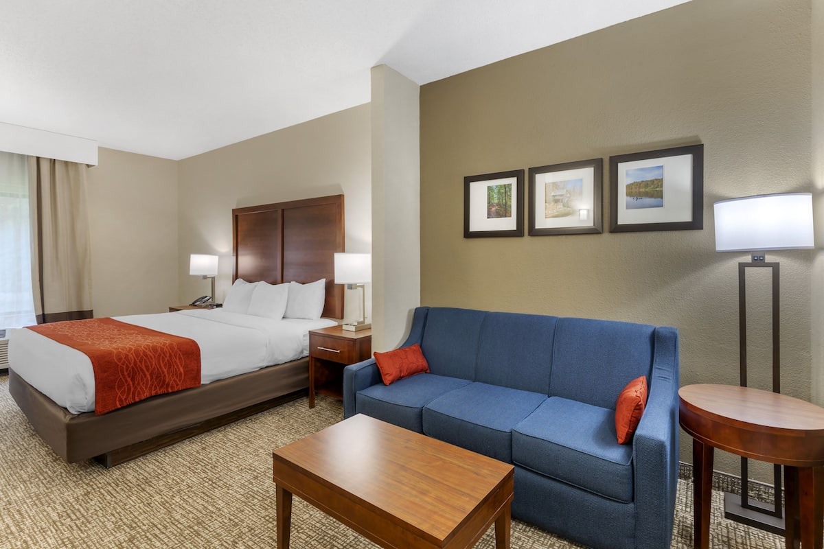A hotel room with a bed, a blue sofa, a wooden coffee table, and a small round table.