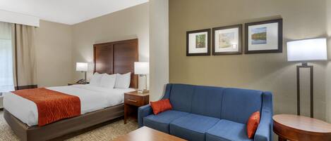 A hotel room with a bed, a blue sofa, a wooden coffee table, and a small round table.