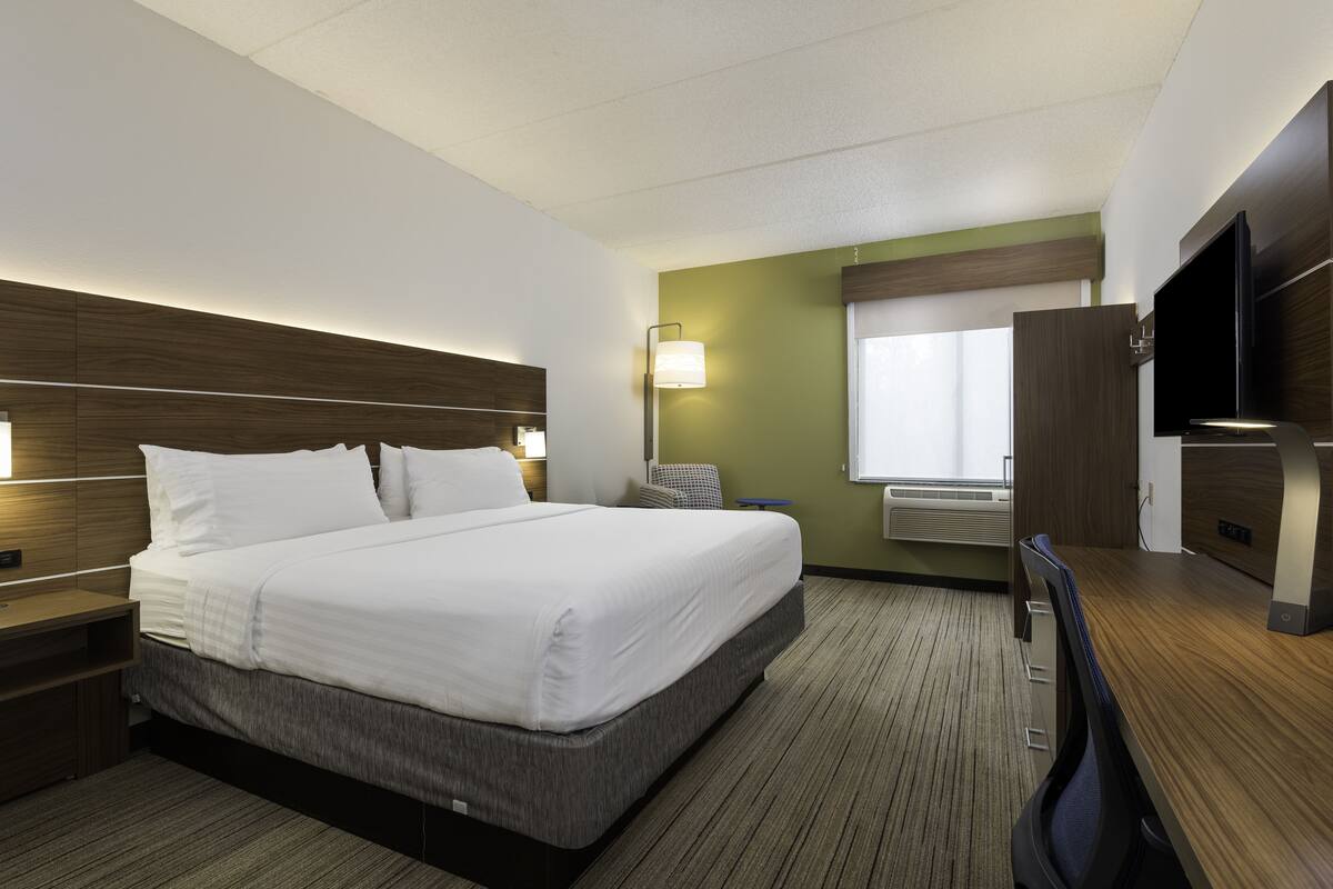 Hotelkamer met een groot bed, bureau, stoel, flatscreen televisie en raam met zonwering.