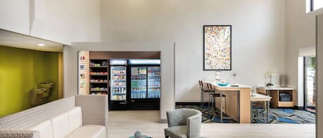 A hotel lobby with seating, a refrigerator stocked with beverages, and a desk area.