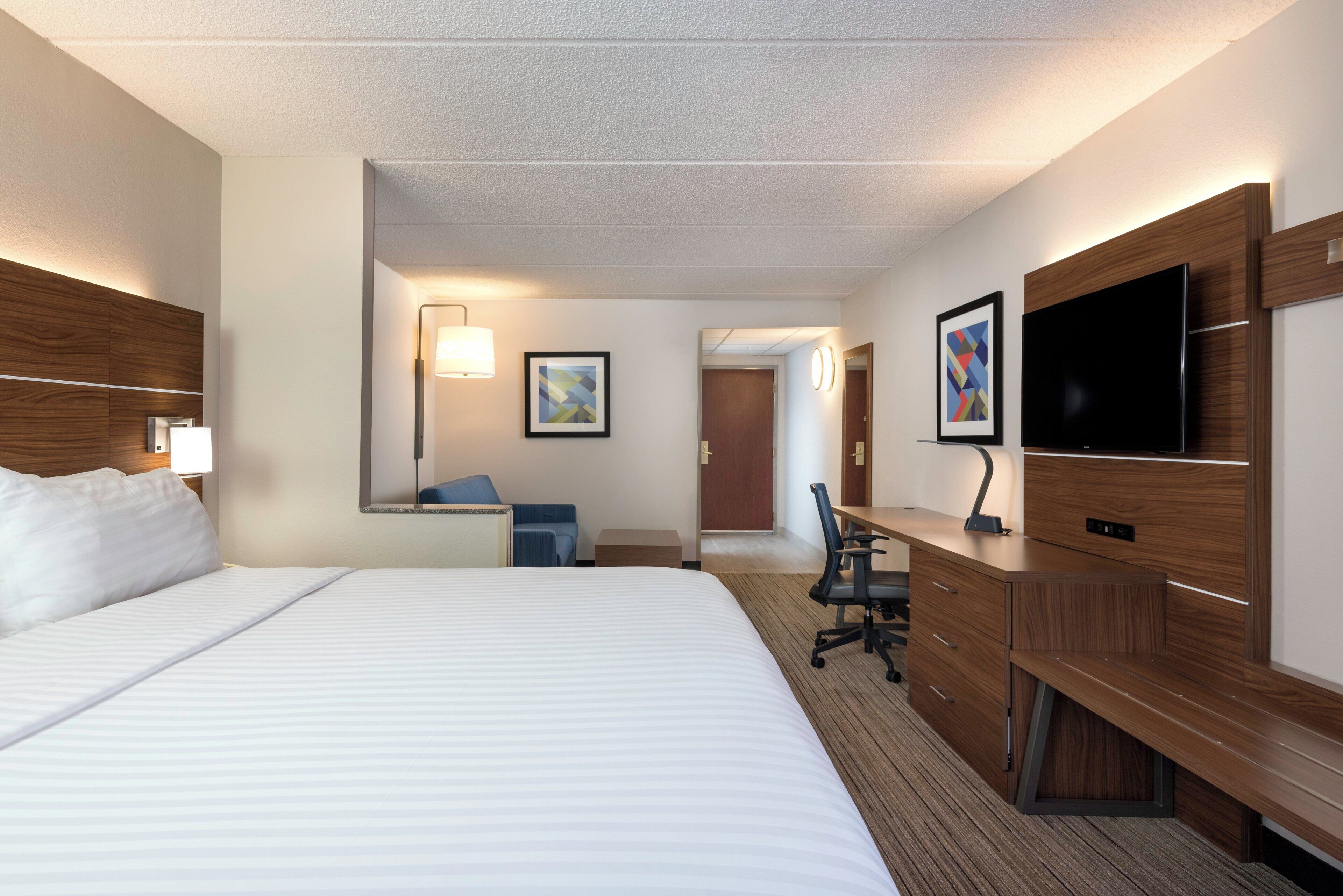 Ett hotellrum med en stor säng, ett skrivbord med en stol, en tv och en spegel.