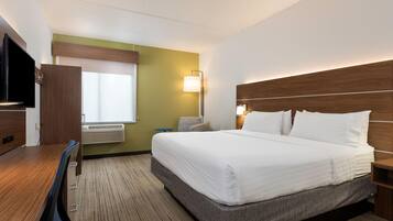 A hotel room with a large bed, a desk, a chair, a television, and a window.