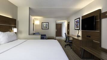 A hotel room with a large bed, a desk with a chair, a flat-screen TV, and a mirror.