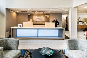A hotel reception area with a reception desk, a receptionist, and a coffee station. - Holiday Inn Express & Suites Charlotte Arpt-Belmont by IHG (Belmont)