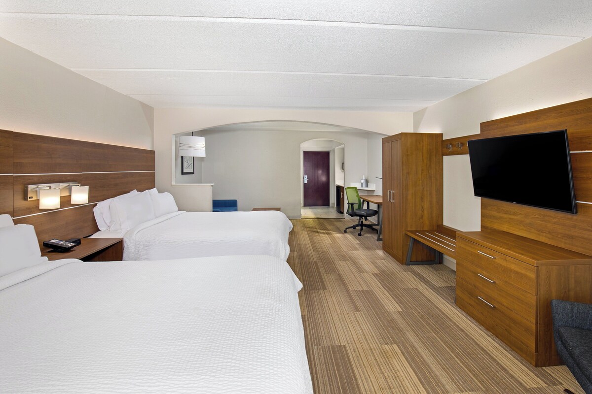 Habitació d'hotel amb dos llits, una televisió, una taula de treball i un bany visible a través d'una galeria.