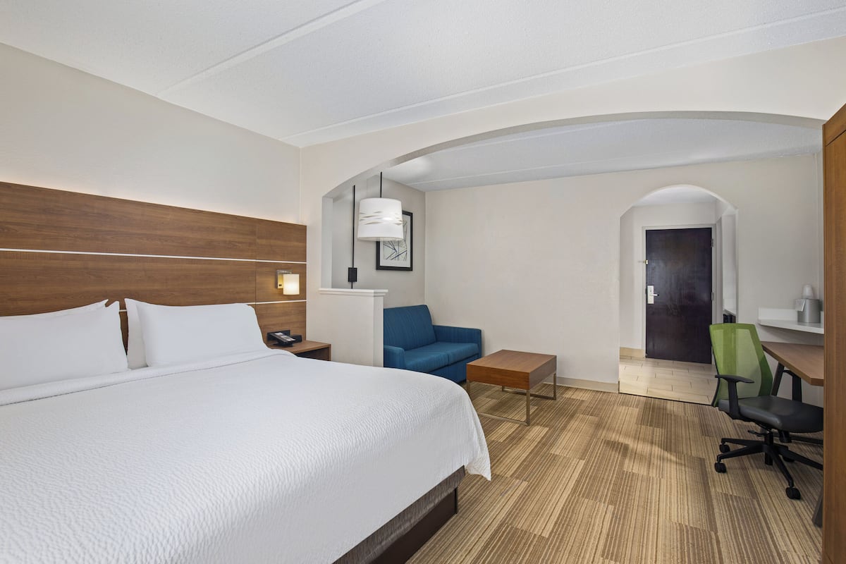 A hotel room with a large bed, a blue sofa, a desk, and a green office chair.