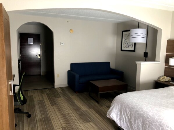 A hotel room with a sofa, a small table, a bed, a desk, and a lamp. - Holiday Inn Express Hotel and Suites Kings Mountain by IHG (Kings Mountain)
