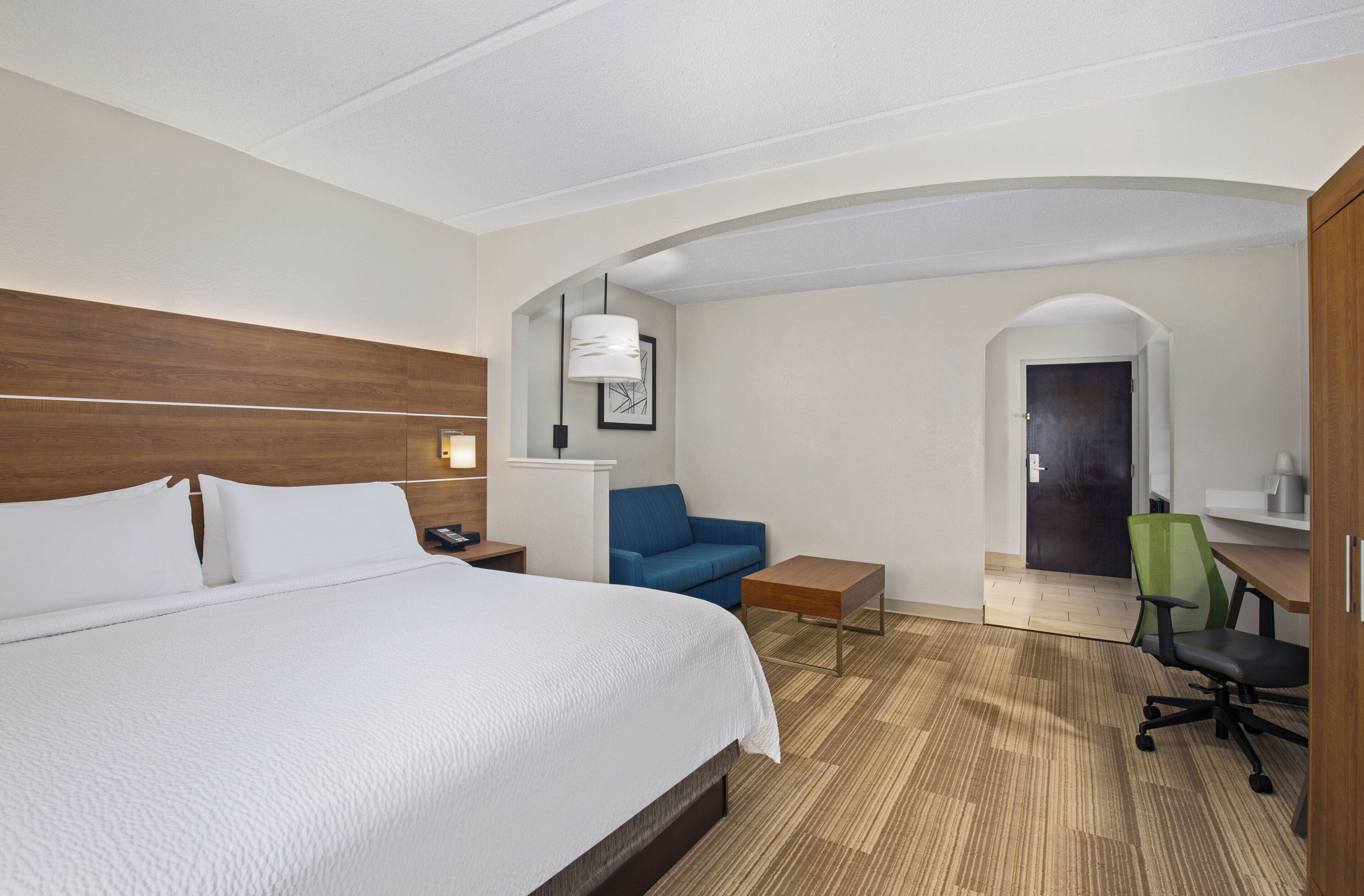A hotel room with a large bed, a blue sofa, a desk, and a green office chair.