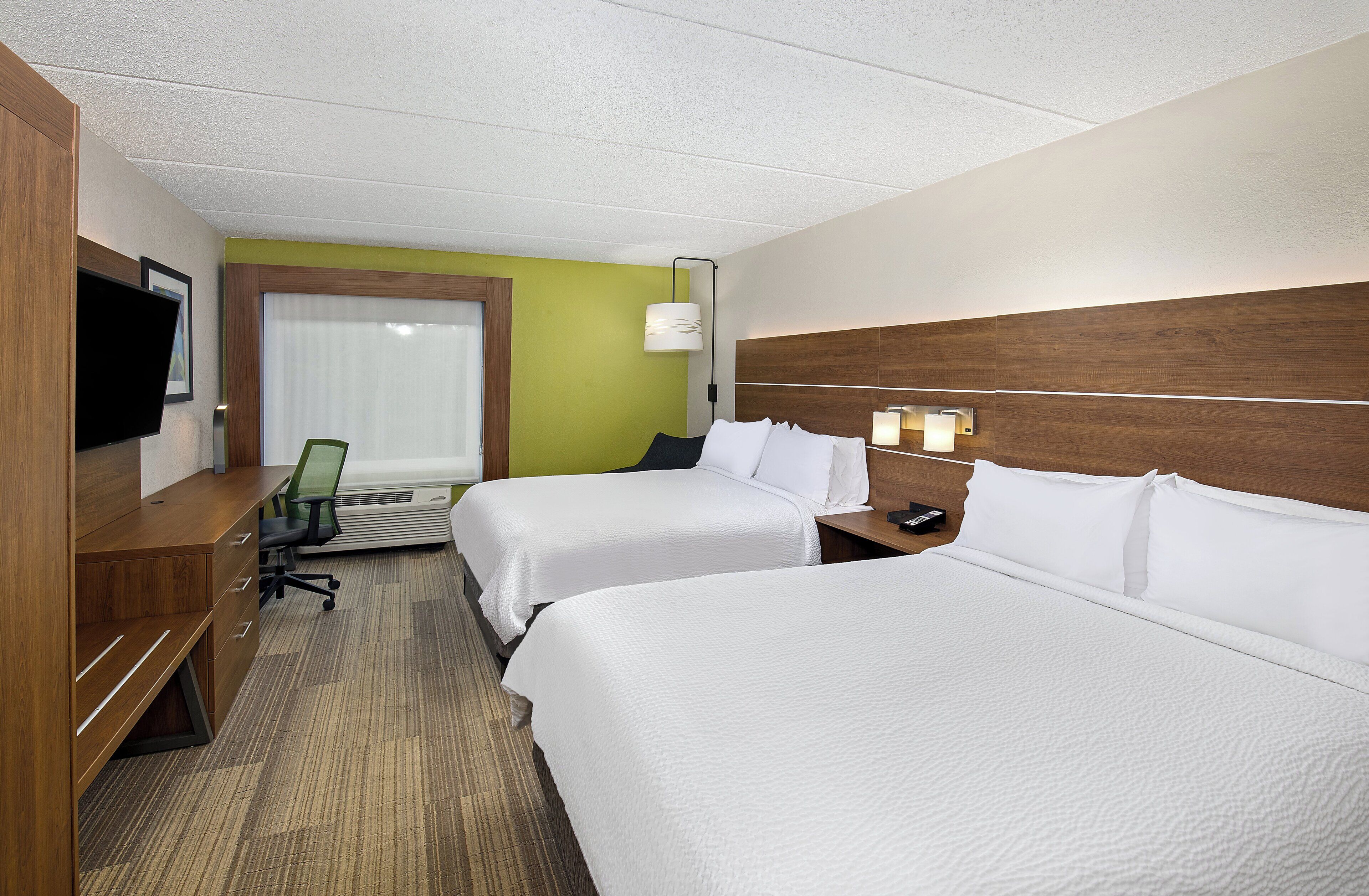 Habitación de hotel con dos camas, un escritorio con silla, televisión y ventana con persianas.