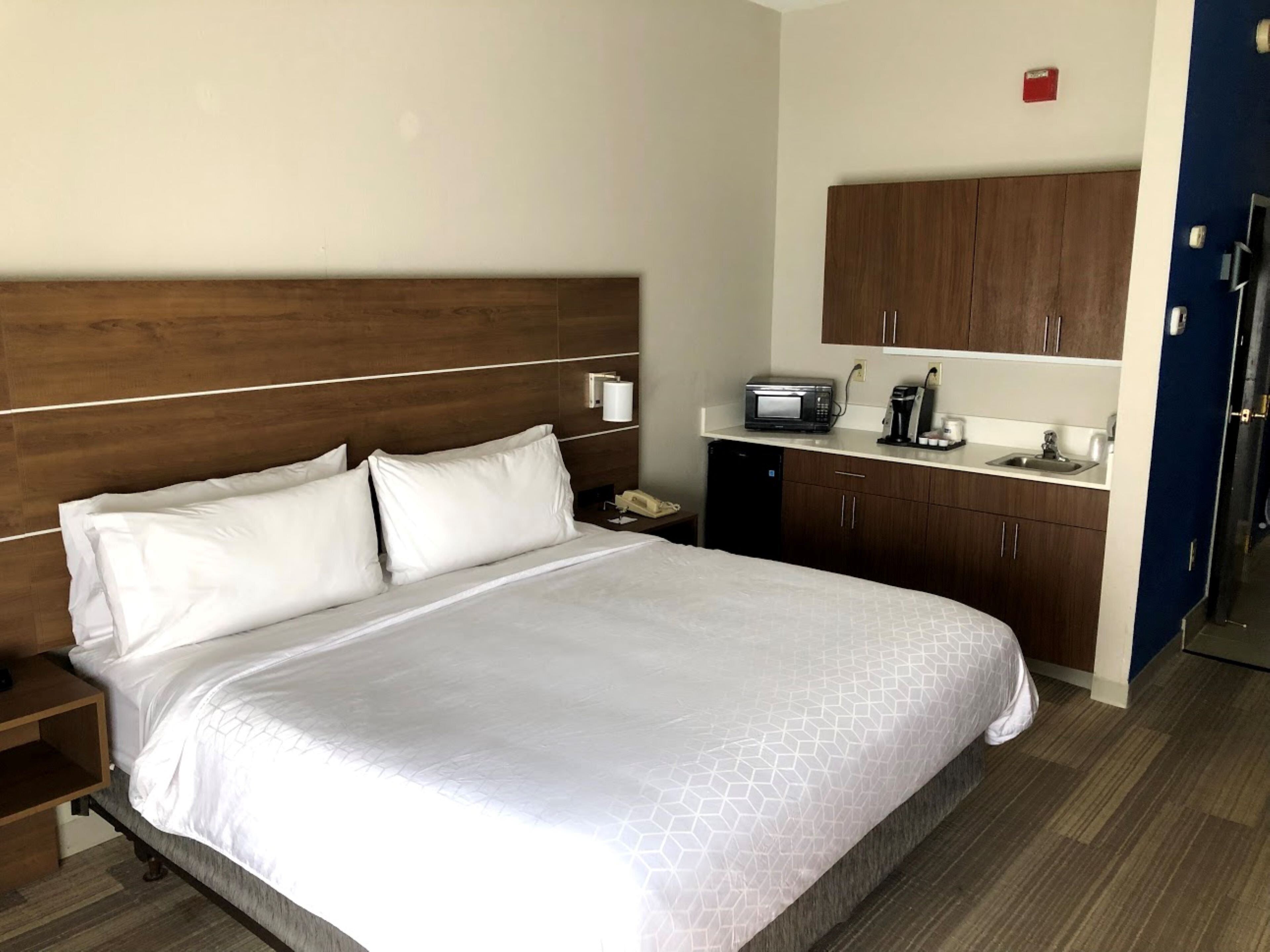 A hotel room with a bed, a nightstand, a microwave, a coffee maker, and a small refrigerator.