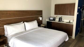 A hotel room with a bed, a nightstand, a microwave, a coffee maker, and a small refrigerator.