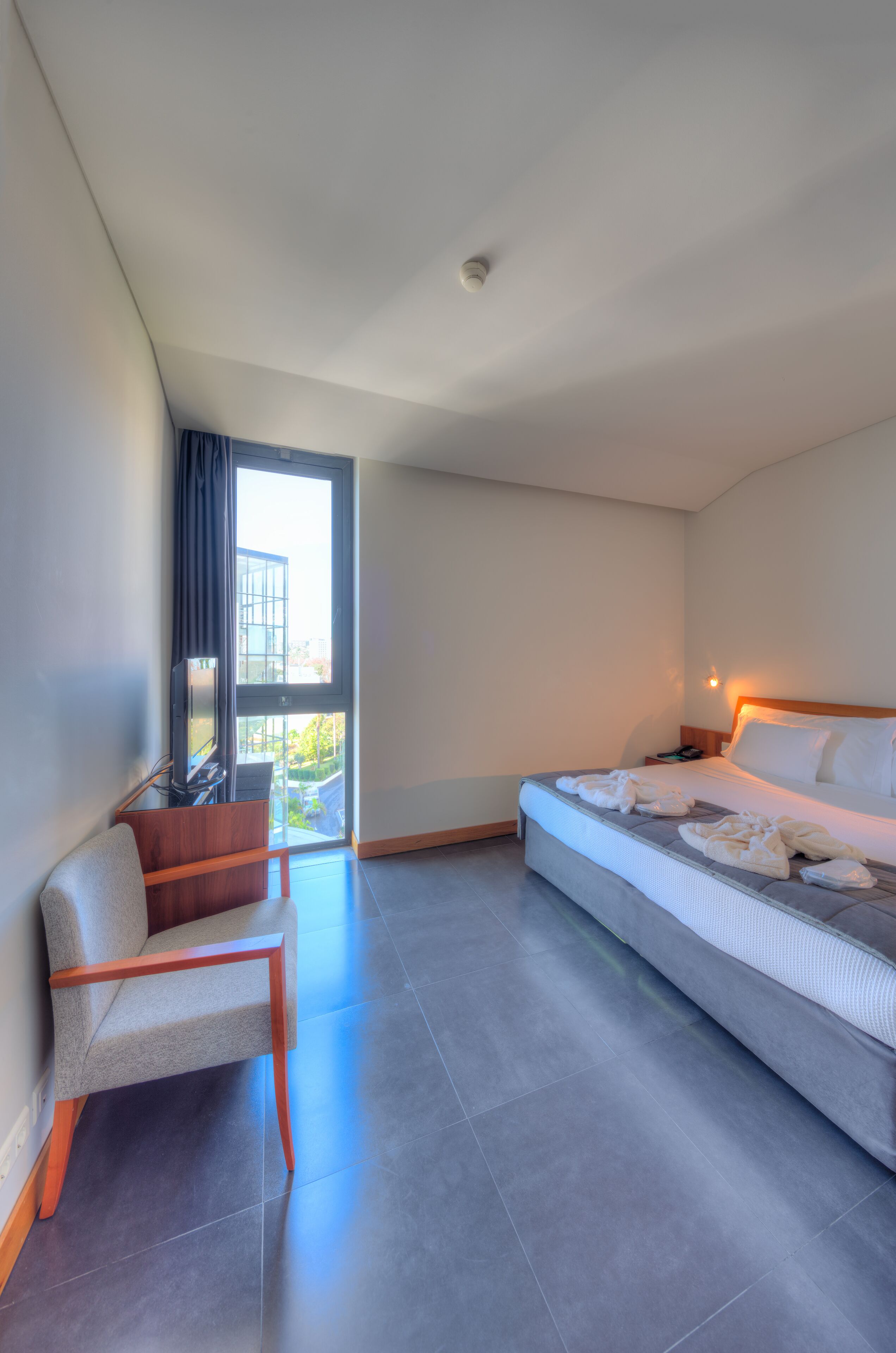 Ein modernes Hotelzimmer mit Bett, Sessel, Fernseher und Balkonblick.